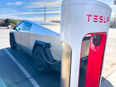 Mesquite, Nevada, ABD-10 Kasım 2024 - Tesla Cybertruck 'ın bir Tesla Superşarj istasyonuna bağlı yan görüntüsü, açık mavi gökyüzü altında aracın parlak tasarımını gösteriyor. Palmiye ağaçları ve yakınlarda