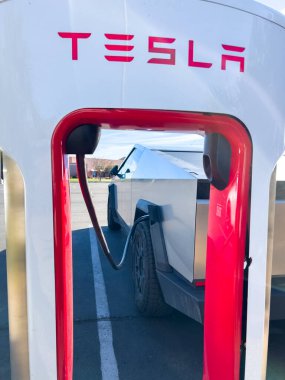 Mesquite, Nevada, ABD-10 Kasım 2024 - Tesla Cybertruck 'ın bir Tesla Superşarj istasyonuna bağlı yan görüntüsü, açık mavi gökyüzü altında aracın parlak tasarımını gösteriyor. Palmiye ağaçları ve yakınlarda