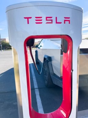 Mesquite, Nevada, ABD-10 Kasım 2024 - Tesla Cybertruck 'ın bir Tesla Superşarj istasyonuna bağlı yan görüntüsü, açık mavi gökyüzü altında aracın parlak tasarımını gösteriyor. Palmiye ağaçları ve yakınlarda