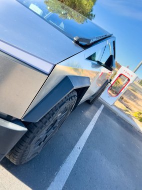 Mesquite, Nevada, ABD-10 Kasım 2024 - Tesla Cybertruck 'ın bir Tesla Superşarj istasyonuna bağlı yan görüntüsü, açık mavi gökyüzü altında aracın parlak tasarımını gösteriyor. Palmiye ağaçları ve yakınlarda