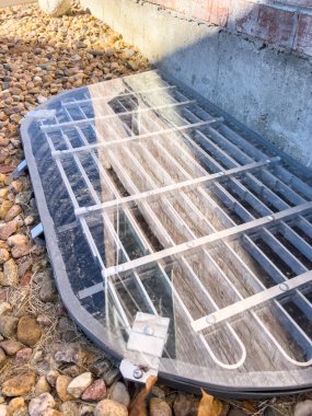 Dekoratif kayalarla çevrili metal bir ızgarayla kaplı koruyucu bir pleksiglas pencere, sonbahar sezonunun sonlarında bahçedeki tuğladan bir duvara dayanıyor..