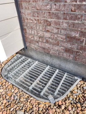 Dekoratif kayalarla çevrili metal bir ızgarayla kaplı koruyucu bir pleksiglas pencere, sonbahar sezonunun sonlarında bahçedeki tuğladan bir duvara dayanıyor..