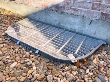 Dekoratif kayalarla çevrili metal bir ızgarayla kaplı koruyucu bir pleksiglas pencere, sonbahar sezonunun sonlarında bahçedeki tuğladan bir duvara dayanıyor..