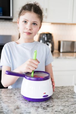 Odaklanmış bir dikkatle, bu filizlenen aşçılık sanatçısı krakerleri erimiş çikolataya batırarak iyi aydınlatılmış bir ev mutfağının sıcaklığında tatlı tatlar yaratıyor..