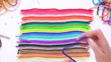 Düz yatıyordu. Sanatsal eller, beyaz arkaplanın altındaki organize katmanlarla çelişen parlak renkli kil boncuk kablolarından oluşan bir seçimi kaldırır..