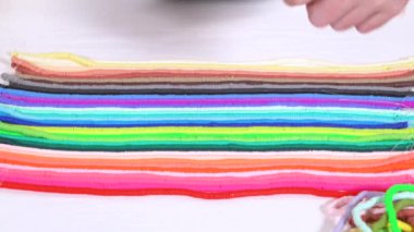 Eller birbirine zıt beyaz bir yüzeye karşı düzgün düzenlenmiş renkli, sarmalanmış kil boncuk iplikçiklerine dokunur..