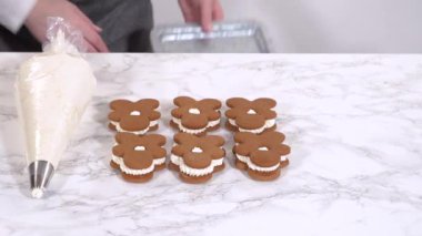 Zencefilli kurabiyeler mermer yüzeyde ikinci yarılarını beklerler, her biri lezzetli sandviçler yapmak için tereyağlı kremayla titizlikle borular. Boruların hassasiyeti şenlikli bir dokunuş katıyor..