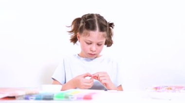 Genç kız derinden bilezik yapma sanatına odaklanmış. Canlı kil boncukları eşsiz kalıplara döküyor. Çalışma alanı çeşitli boncuklarla düzenlenmiş. Bu da nişanını gösteriyor.