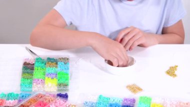 Genç kız derinden bilezik yapma sanatına odaklanmış. Canlı kil boncukları eşsiz kalıplara döküyor. Çalışma alanı çeşitli boncuklarla düzenlenmiş. Bu da nişanını gösteriyor.