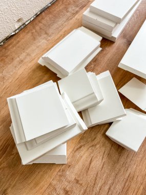 A pile of freshly cut white baseboards placed on vinyl plank flooring, prepared for installation during a home improvement project. clipart