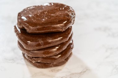 Multiple discs of Chocolate Gingerbread Cookie Dough wrapped in plastic wrap, stacked and ready to chill. These dough discs make it convenient to shape cookies for holiday baking. clipart