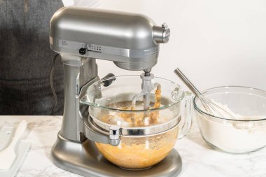 Karıştırma kabında Amber Zencefilli Kurabiye Hamuru 'nun malzemelerinin bulunduğu bir tezgahın yan görüntüsü, mermer tezgahın üzerine yerleştirilmiş, yakınlardaki ıslak malzemelerle dolu ayrı bir kase,