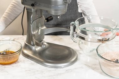 Side view of a stand mixer with a large glass bowl and separate bowls of wet and dry ingredients, ready for mixing into Chocolate Ginger Sugar Cookie Dough. clipart