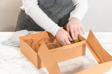 Kurulum sürecinde, bir kadın bu şarküteri kutusunu ustalıkla düzenliyor, dilimlenmiş et, peynir, kraker ve üzüm sergiliyor, hepsi düzgünce düzenlenmiş ve kahverengi bir hediye kutusunda paketlenmiş..