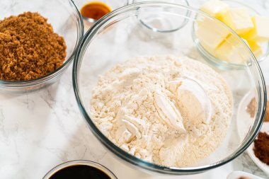 Arka planda ana zencefilli ekmek baharatları, tereyağı ve yumurtalarla dolu bir cam karıştırma kabının genel manzarası. Bu malzemeler klasik zencefilli çöreğin yapımında kullanılacak.