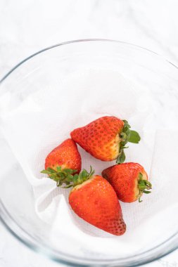 Parlak kırmızı çilekler, küf izleriyle karışmış, beyaz peçetedeki kağıt havluyla kaplı cam bir kasede dinleniyor, depolama tekniklerini gösteriyor..