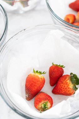 Parlak kırmızı çilekler, küf izleriyle karışmış, beyaz peçetedeki kağıt havluyla kaplı cam bir kasede dinleniyor, depolama tekniklerini gösteriyor..