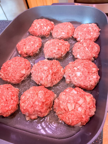 Close-up of raw homemade katleti patties made with minced meat and diced onions, arranged in an oiled pan. Traditional Slavic comfort food ready to be cooked.