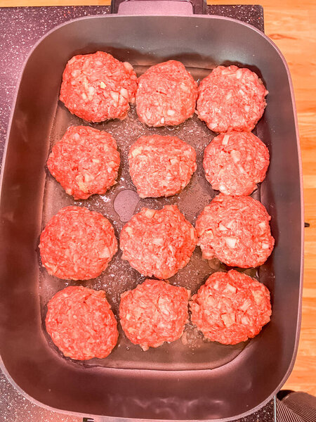 Close-up of raw homemade katleti patties made with minced meat and diced onions, arranged in an oiled pan. Traditional Slavic comfort food ready to be cooked.