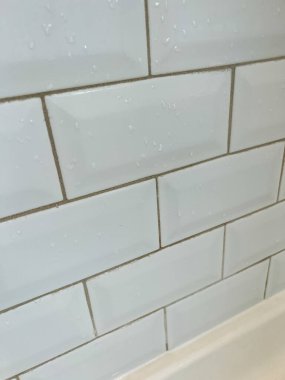 Banyodaki beyaz bir metro fayans duvarının yakın görüntüsü. Temiz kiremitler ve sıva demiri var. Yüzey küçük su damlacıklarını gösteriyor, son kullanım ve harç ihtiyacını vurguluyor
