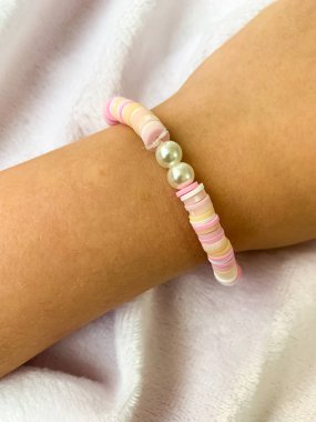 Küçük bir kız bileğinde el yapımı inci bileziğini gösteriyor. Basit ama zarif bilezik beyaz boncuklarla yaratıcılığı ve işçiliği ön plana çıkarıyor..