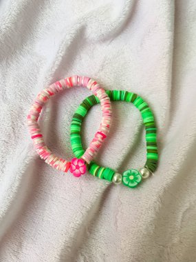 A handmade bracelet crafted with pink, purple, and white beads displayed on a soft white fabric. This colorful accessory highlights creativity and craftsmanship, perfect for kids jewelry or DIY clipart