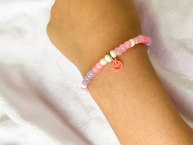 Küçük bir kız bileğinde el yapımı inci bileziğini gösteriyor. Basit ama zarif bilezik beyaz boncuklarla yaratıcılığı ve işçiliği ön plana çıkarıyor..