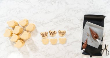 Kraliyet Buzlanma Tarifi ile Panda Yüzleri Dekorasyonu: Kurabiyelerin üzerindeki el borularıyla pandanın yüzlerini çikolatayla süsleyen, dekorasyon sürecini vurgulayan.