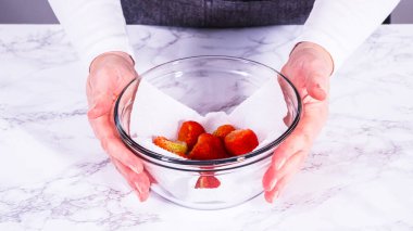 Çilekler, yeni yıkanmış ve kurutulmuş, cam bir kasede güzelce depolanmış kağıt havluyla kaplanmış ve tazeliği korumak için plastikle kaplanmış..