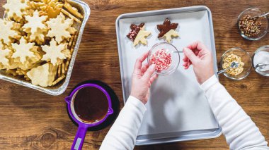 Flat lay. Creating snowflake-shaped cutout sugar cookies, dipped in chocolate, and adorned with different toppings. clipart