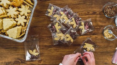 Flat lay. Carefully packaging Christmas cutout cookies, half-dipped in chocolate, sprinkled with crushed nuts, and presented in clear cellophane wrapping. clipart