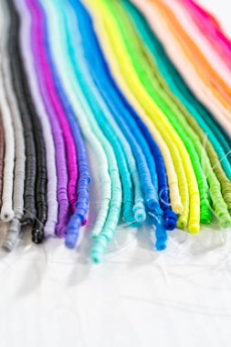 Beyaz bir masadaki renklere göre düzenlenmiş canlı bir kil boncuk koleksiyonu genç zanaatkarlara kendi eşsiz bileziklerini yapmaları için ilham vermeye hazır..