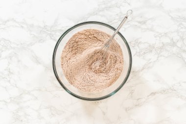 Zencefilli Ginger Şekerli Kurabiye Hamuru için un ve baharat içeren bir kasenin üst görüntüsü, zencefil ve kakao tozu gibi anahtar içerikleri vurguluyor..