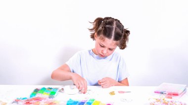 Genç bir kızın narin parmakları parlak, renkli boncuklardan oluşan bir hazinede geziniyor. Her bölümde seçilecek yeni bir renk var. Neşeli bir vazifeye daldı.