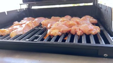 Salamura edilmiş tavuk butları küçük bir Weber ızgarasının ızgarasında cızırdar, havayı iştah açıcı bir koku ve hafif bir dumanla doldurur..