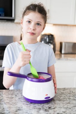 Odaklanmış bir dikkatle, bu filizlenen aşçılık sanatçısı krakerleri erimiş çikolataya batırarak iyi aydınlatılmış bir ev mutfağının sıcaklığında tatlı tatlar yaratıyor..