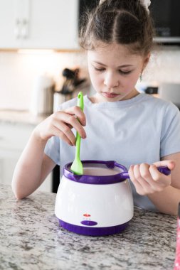 Odaklanmış bir dikkatle, bu filizlenen aşçılık sanatçısı krakerleri erimiş çikolataya batırarak iyi aydınlatılmış bir ev mutfağının sıcaklığında tatlı tatlar yaratıyor..