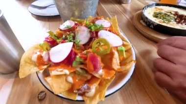 Castle Rock, Colorado, 12 Mayıs 2024 'te yavaş çekimde bir elin restoran masasındaki bir tabaktan taco alırken görüntüsü. Sahnede çeşitli renkli ve iştah açıcı yemekler var.