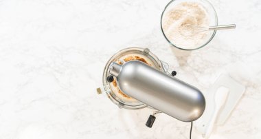 Overhead view of a baking setup for Classic Gingerbread Cookie Dough, with a stand mixer surrounded by essential ingredients. Ingredients include brown sugar, butter, flour mixture, and dark molasses clipart