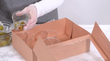 Elleri titizlikle bir kaseye taze kırmızı üzüm ekliyor, çeşitli peynirler, zeytinler ve pişirilmiş etlerle dolu güzel bir şarküteri kutusunu tamamlıyor.