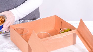 Elleri titizlikle bir kaseye taze kırmızı üzüm ekliyor, çeşitli peynirler, zeytinler ve pişirilmiş etlerle dolu güzel bir şarküteri kutusunu tamamlıyor.