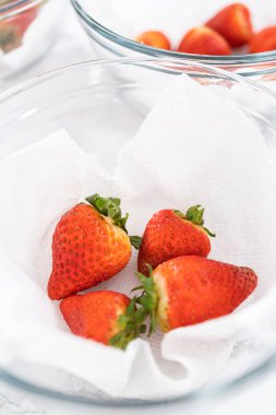 Parlak kırmızı çilekler, küf izleriyle karışmış, beyaz peçetedeki kağıt havluyla kaplı cam bir kasede dinleniyor, depolama tekniklerini gösteriyor..