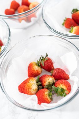 Parlak kırmızı çilekler, küf izleriyle karışmış, beyaz peçetedeki kağıt havluyla kaplı cam bir kasede dinleniyor, depolama tekniklerini gösteriyor..