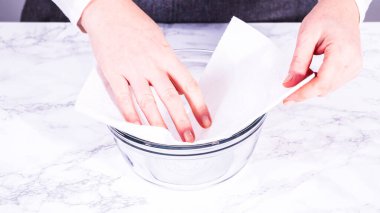 Çilekler, yeni yıkanmış ve kurutulmuş, cam bir kasede güzelce depolanmış kağıt havluyla kaplanmış ve tazeliği korumak için plastikle kaplanmış..