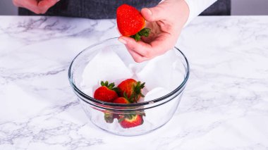 Çilekler, yeni yıkanmış ve kurutulmuş, cam bir kasede güzelce depolanmış kağıt havluyla kaplanmış ve tazeliği korumak için plastikle kaplanmış..