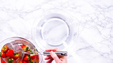 Düz yatıyordu. Olgun çilekler, depolama veya tüketimden önce temizlik ve uzun ömürlü olmak için meyveyi yıkamada bir adım olarak büyük bir bardakta karıştırma kabında suya gömülür..