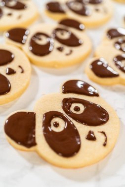 Overhead view of a batch of panda cookies with completed chocolate icing designs for the Chocolate Royal Icing Recipe. Each cookie features a cute panda face, giving a uniform and adorable look. clipart