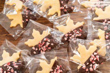 Dikkatlice paketlenmiş Noel kurabiyeleri, çikolataya batırılmış ve şeffaf selofan ambalajla sunulmuş, bayram hediyesi olarak mükemmel..