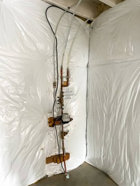 Castle Pines, Colorado ABD - 18 Ocak 2023 'te yeni bir inşaat evinin bodrumunda bir tesisat kurulumu görüldü. Sistem beyaz plastik buharla kaplı bir duvara dayanıyor.