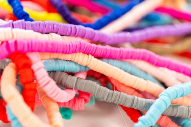 Beyaz bir masadaki renklere göre düzenlenmiş canlı bir kil boncuk koleksiyonu genç zanaatkarlara kendi eşsiz bileziklerini yapmaları için ilham vermeye hazır..